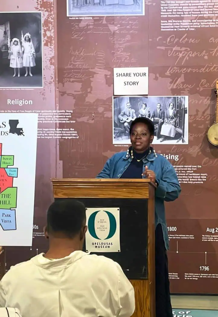 Divine Bailey-Nicholas speaks at a podium inside the Opelousas Museum, surrounded by historical exhibits and photographs.